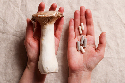 a hand holding a king oyster mushrooms and another hand holding mushroom supplements